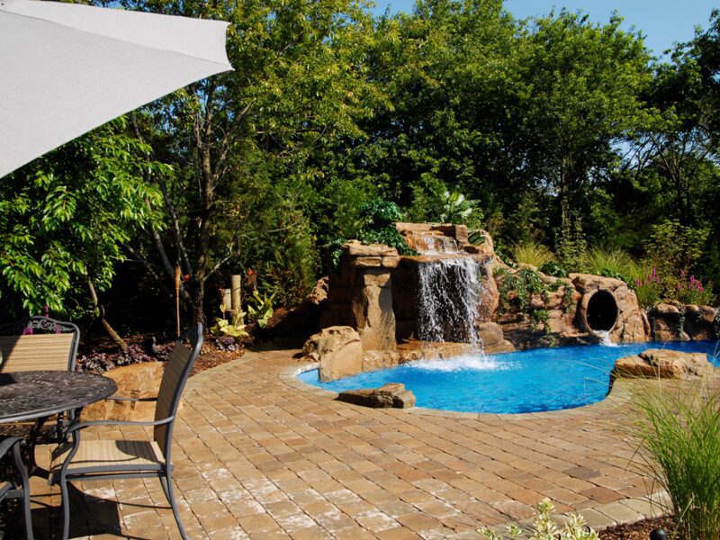 A pool with an umbrella and waterfall in the middle of it.