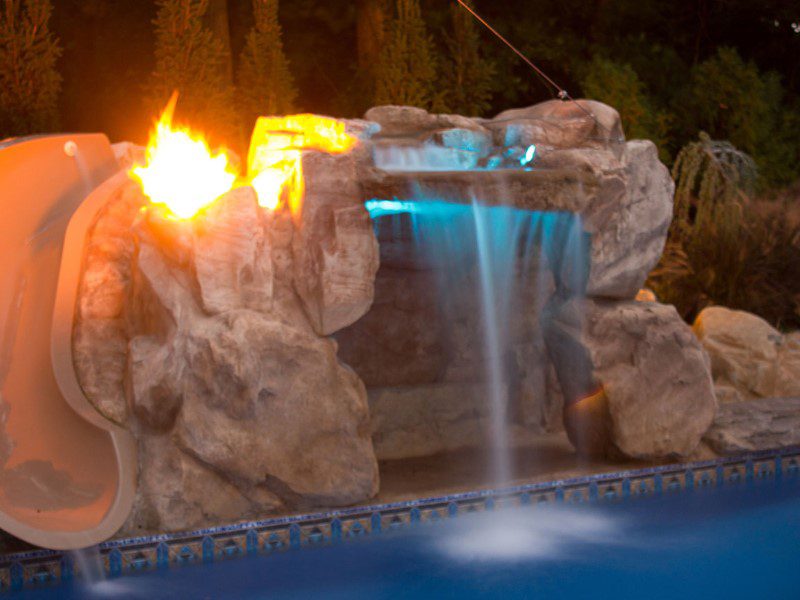 A pool with a waterfall and fire in the background.