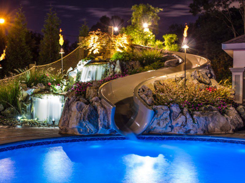 A pool with water slides and lights at night.