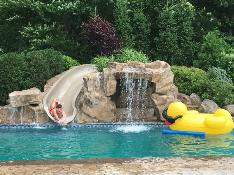A man is sliding down the slide in his pool.