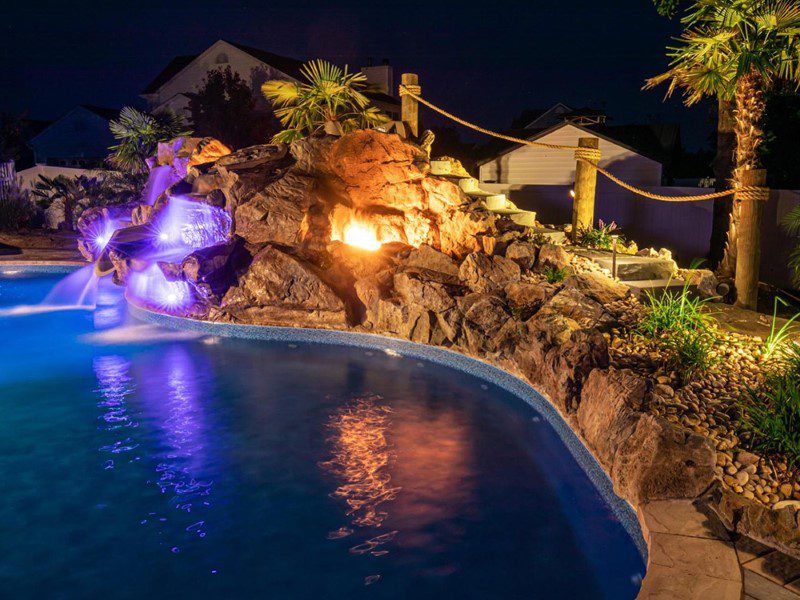 A pool with lights on and rocks in the background