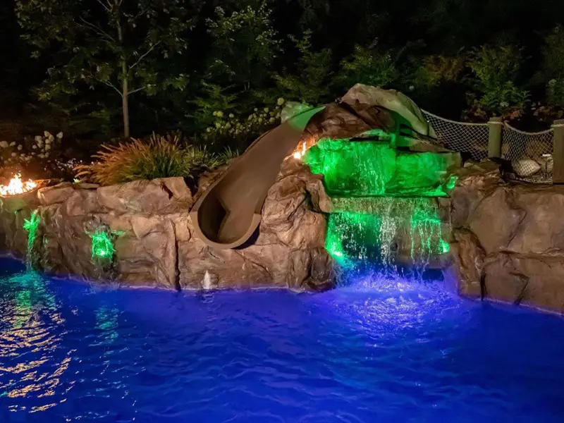A pool with a slide and waterfall at night.