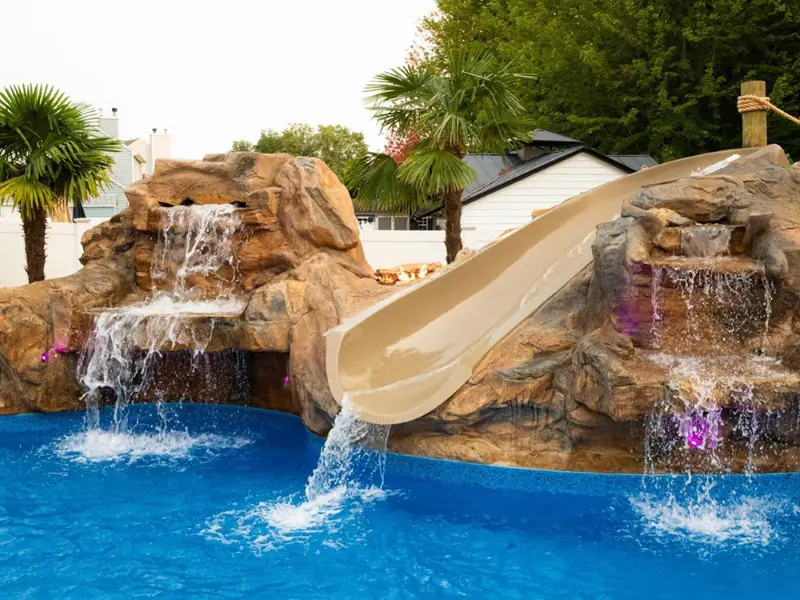 A pool with water slide and rocks in the middle of it
