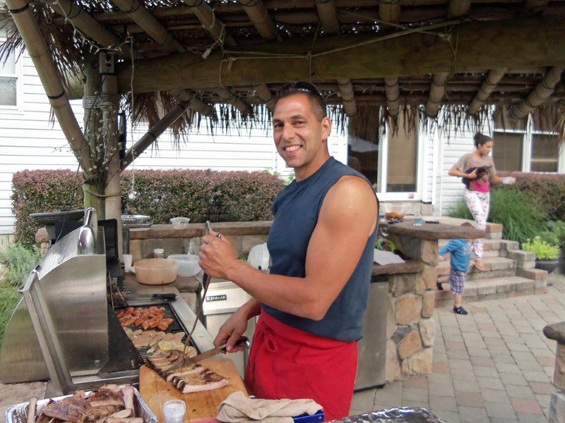 A man standing next to a grill with food on it.