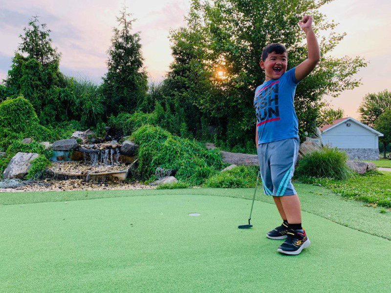 A boy is holding his arms up while playing golf.