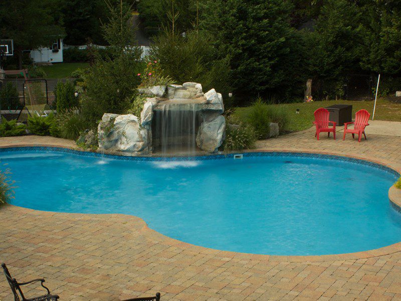 A pool with a waterfall and a brick patio.