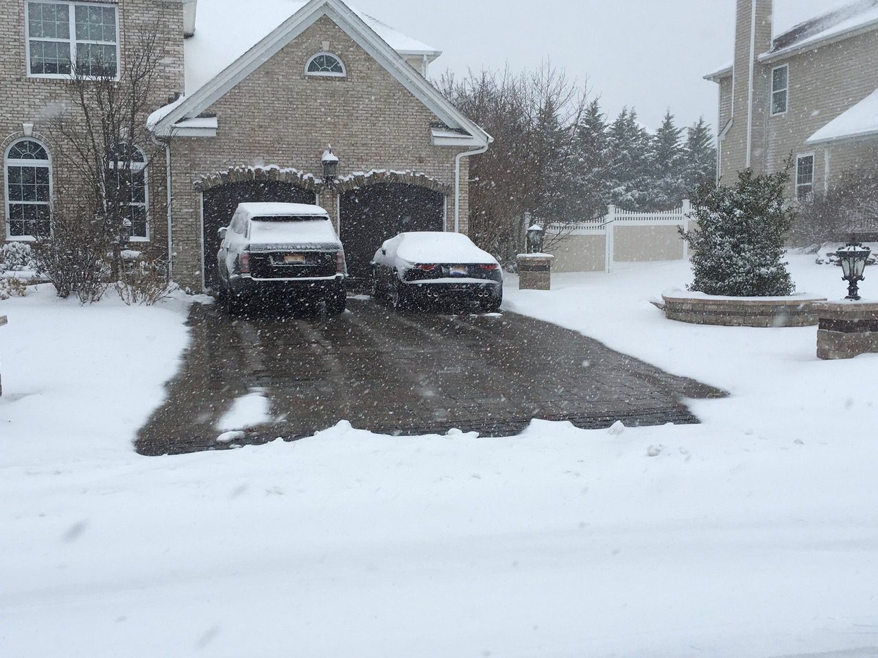 Two cars parked in a driveway covered with snow.