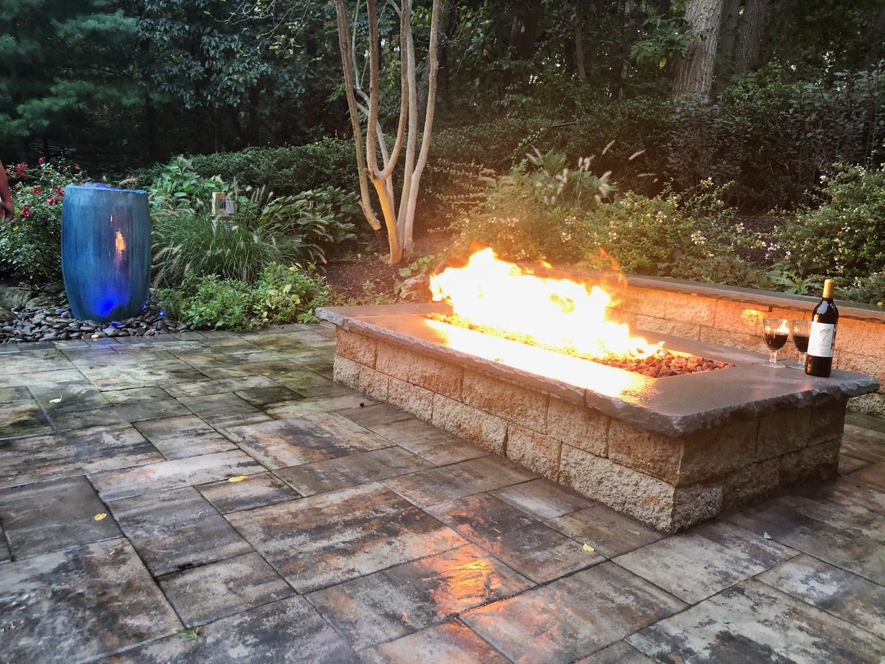 A fire pit is lit on the side of a patio.