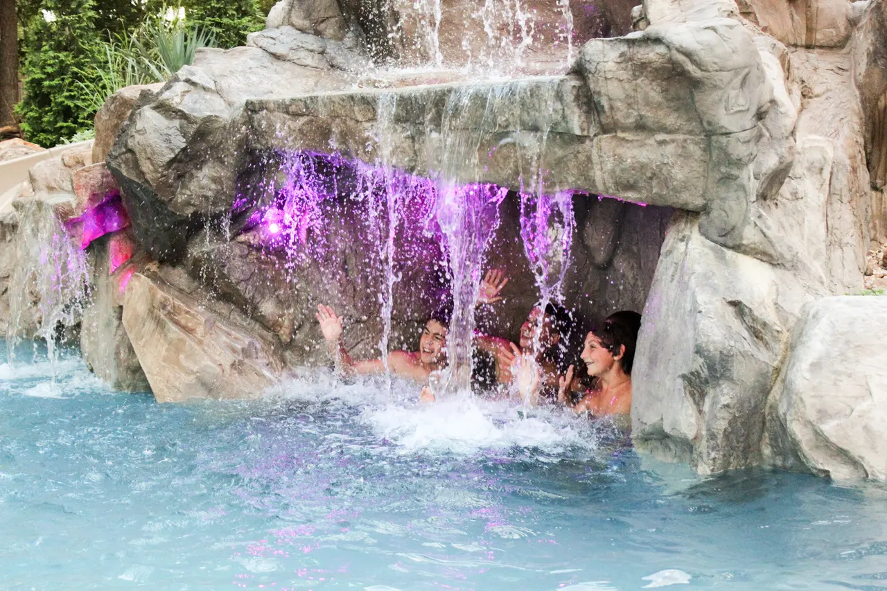 A group of people in the water under a waterfall.