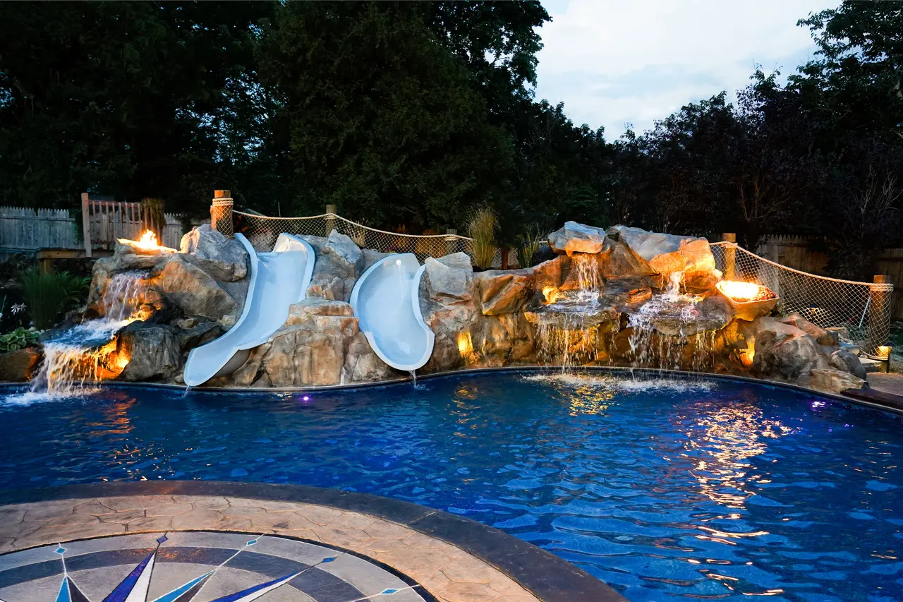 A pool with water slides and rocks in the background.