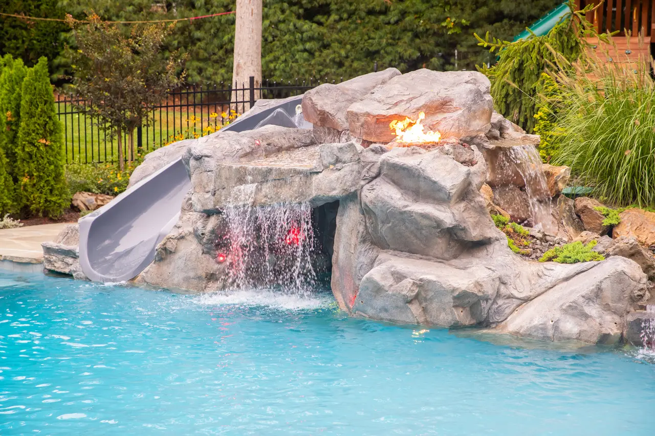 A pool with a slide and rock waterfall.