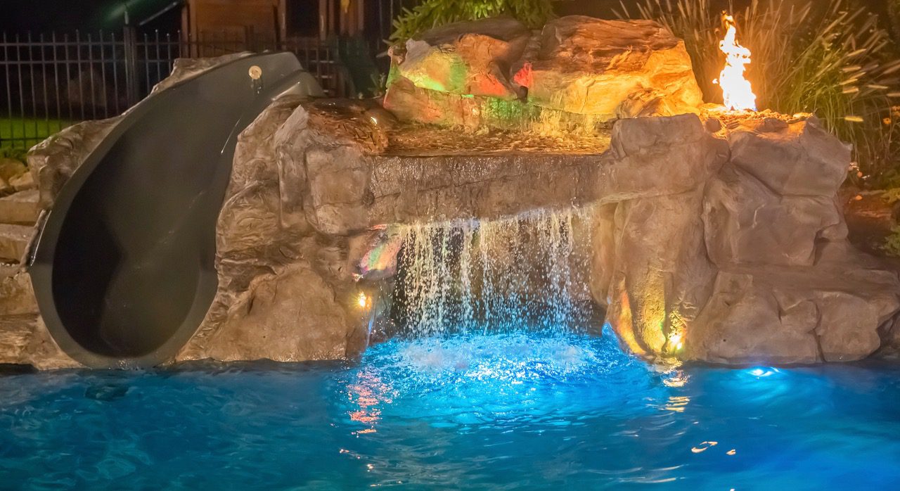 A pool with a waterfall and lights on.