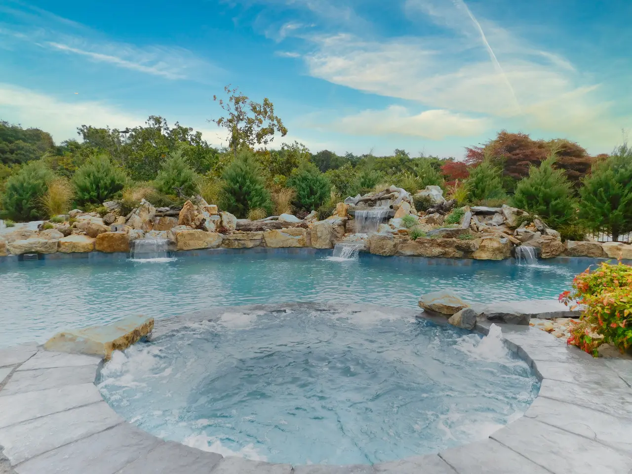 A pool with water flowing around it and trees in the background.