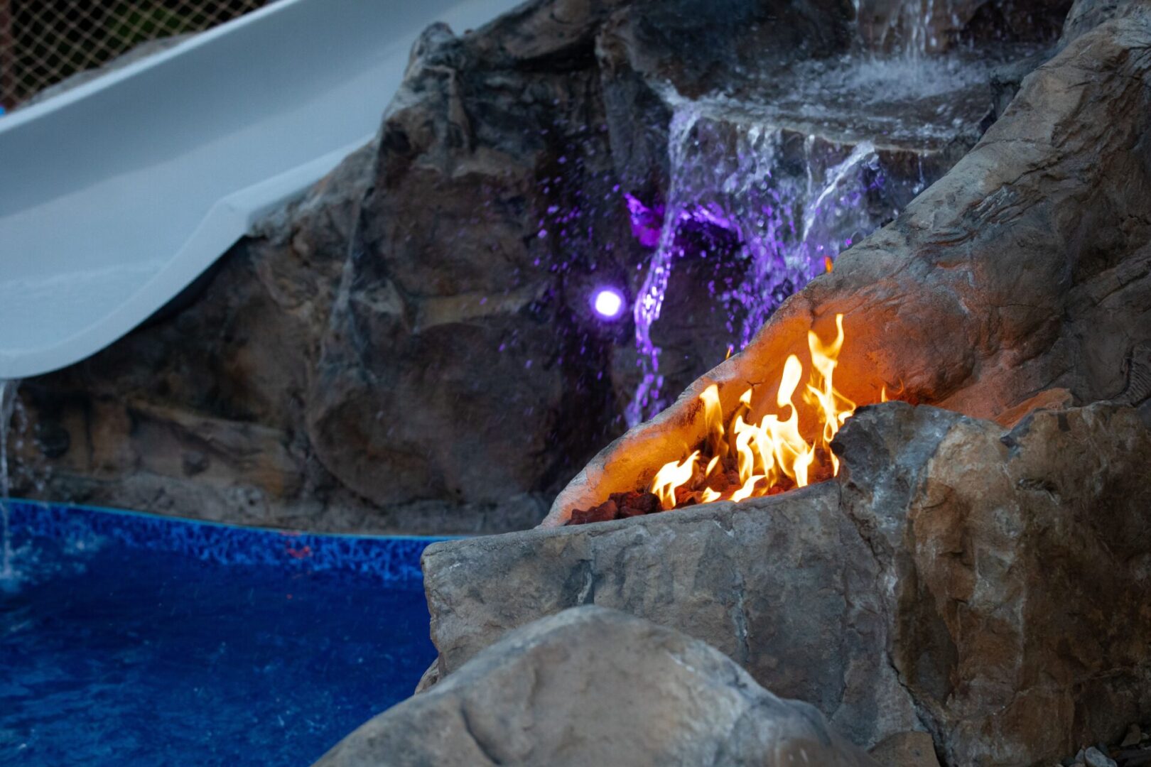 A fire pit with purple lights and water slide.