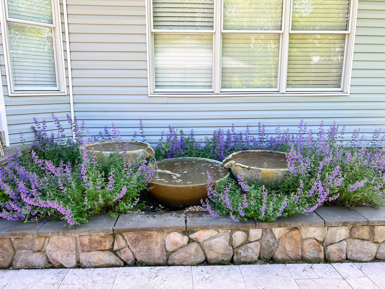A stone wall with three pots and some purple flowers.