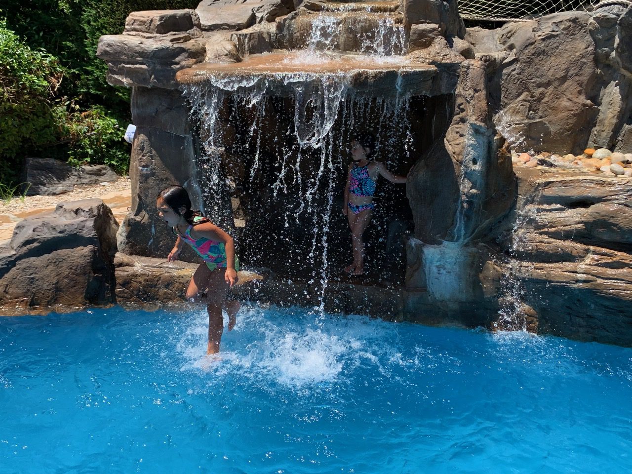 Two people jumping in a pool with water falling from the top of a waterfall.