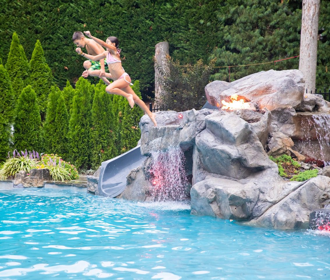 Two people jumping off a pool into the water.