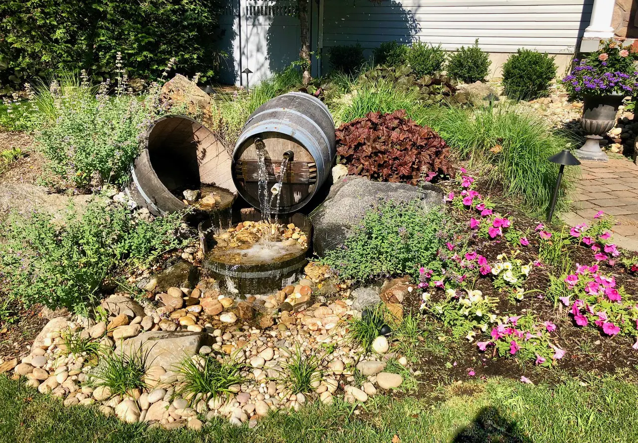 A garden with flowers and plants, rocks and barrels.